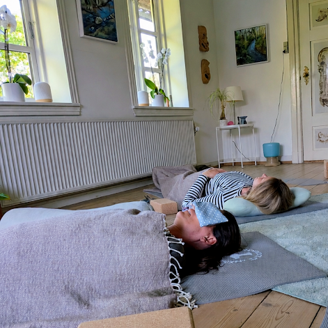 Deltagere ligger til afslapning på måtter i en lys og rolig stue
